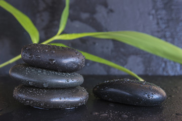 Obraz na płótnie Canvas spa concept/black massage stones and bamboo leaves on black slate background with water drops