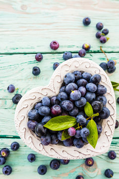 Fresh blueberries in a bowl in the shape of a heart on a wooden background.