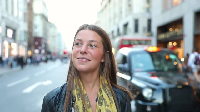 Portrait of a young woman in London. Smiling girl looking at camera in London city centre, with blurred people and traffic on background. Slow motion technique.