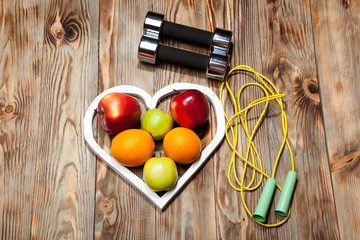 White heart, apples and oranges, healthy diet, dumbbells  a jump rope on  wooden background