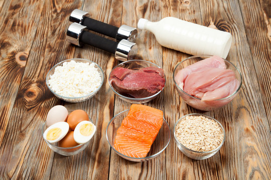 Protein, fish, cheese, eggs, meat, chicken and dumbbells on a wooden background