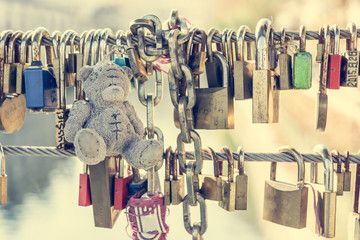 Teddy bear with love locks on a metal bridge.