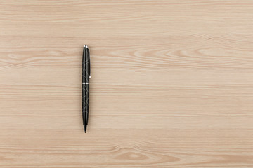 Black ballpoint pen lies on a wooden texture