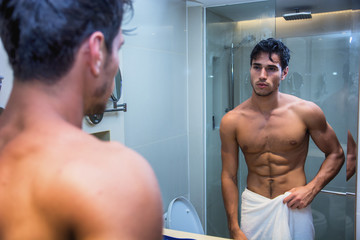 Shirtless muscular handsome young man looking at himself in bathroom mirror in the morning
