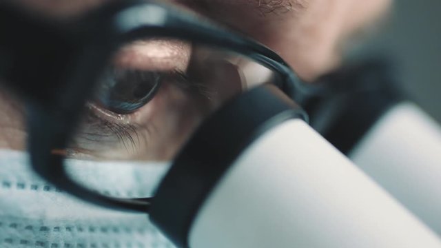 Middle age female scientist in uniform and medical face mask doing microscopic examination in laboratory.