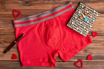 Boxer briefs on wooden background. Fabric hearts near paper bag. Romantic gift for men.