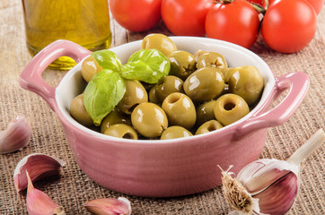 green olive in a pink bowl, garlic, tomatoes and olive oil in a