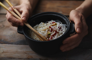 Close up of female hands holding ceramic bowl with noodles dish. 