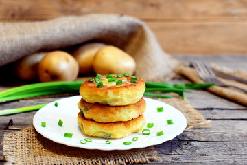 Fried vegetable cutlets. Potato cutlets with vegetables and spices on plate. Raw potatoes, fresh green onions, fork, knife on wooden table. Vintage style. Closeup. Tasty diet recipe