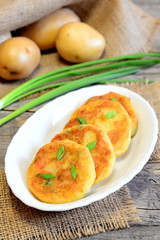 Fried vegetable patties. Potato patties with vegetables and spices on plate and on wooden background. Raw potatoes, fresh green onions. Rustic style. Closeup. Simple vegetarian recipe