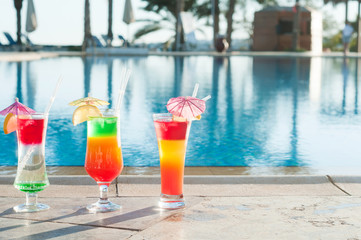 Colored cocktails on a background of water. Colorful cocktails near the pool. Beach party. Summer drinks. Exotic drinks. Glasses of cocktails on table near pool. Summer drinks photo concept. Сocktail