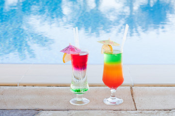 Colored cocktails on a background of water. Colorful cocktails near the pool. Beach party. Summer drinks. Exotic drinks. Glasses of cocktails on table near pool. Summer drinks photo concept. Сocktail