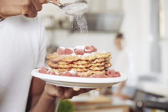Young man sprinkling icing sugar on stack of waffles, close-up