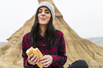 Spain, Navarra, Bardenas Reales, portrait of smiling young woman eating baguette in nature park