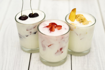 Strawberry, banana and cherry yogurt on a white wooden background. Healthy diet