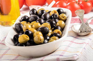 green and black olives in a bowl, tomatoes and olive oil in the