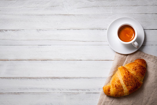cup of espresso coffee with croissant on white wooden table, empty space on left