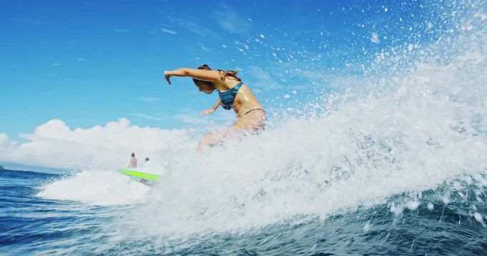 Surfer girl riding wave does turn splashes camera in slow motion. Shot on RED.