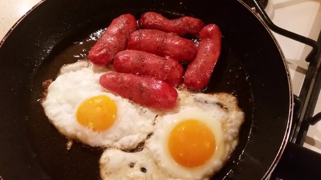 Two eggs and sausages are fried in vegetable oil in a frying pan