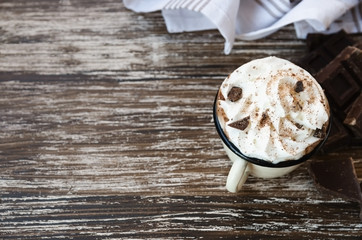 Vintage mug of hot chocolate cocoa with whipped cream and slice of bitter chocolate on wooden background with line napkin. Winter times drink concept. Delicious cold weather beverage. Copy space.