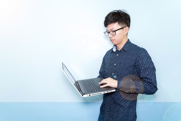 Young asia businessman wear glasses and blue shirt working with laptop on wall background with Lens Flare effect and copy space. Success in business concept. 