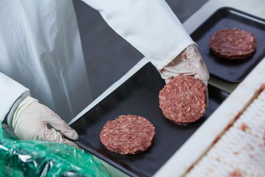 Butcher arranging hamburger patty on tray