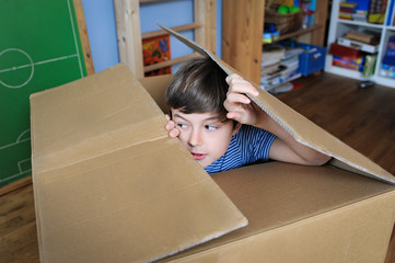 Junge spielt verstecken in einem Pappkarton und schaut aus der Öffnung raus