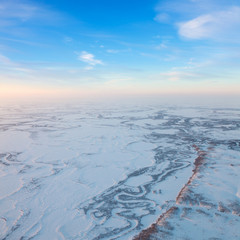 Short winter day above frozen tundra river, top view