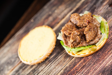 Tasty grilled beef burger with lettuce, ketchup, onion rings, chili and mayonnaise served on pieces of brown paper on a rustic wooden table of counter, with copyspace