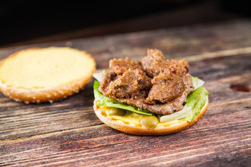 Tasty grilled beef burger with lettuce, ketchup, onion rings, chili and mayonnaise served on pieces of brown paper on a rustic wooden table of counter, with copyspace
