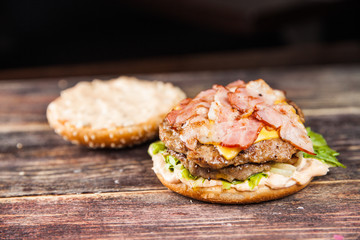 Tasty grilled beef burger with lettuce, ketchup, onion rings, chili and mayonnaise served on pieces of brown paper on a rustic wooden table of counter, with copyspace