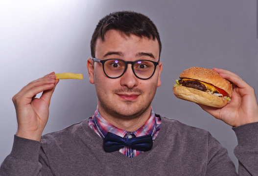 Retrato de un joven nerd con anteojos comiendo hamburguesa.