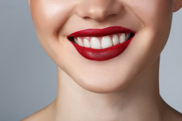 Close-up happy female smile with healthy white teeth, dark red matt lips make-up. Cosmetology, dentistry and beauty care.