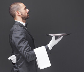 Side view of a waiter in black suit holding a silver tray over d