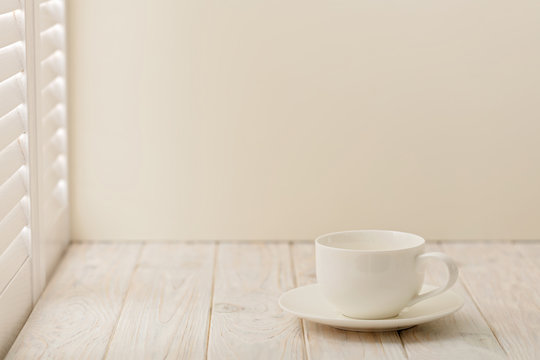 Cup on bright wooden background near a window with shutters.