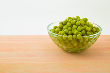 Canned green peas in glass bowl for salad on the table in the kitchen. Healthy eating and lifestyle.