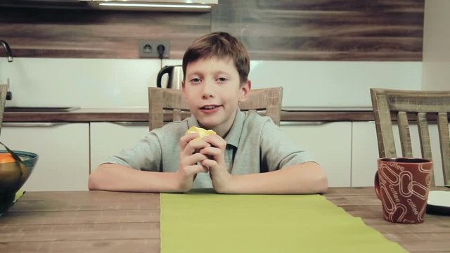 Boy eating an apple sitting at the table at the kitchen