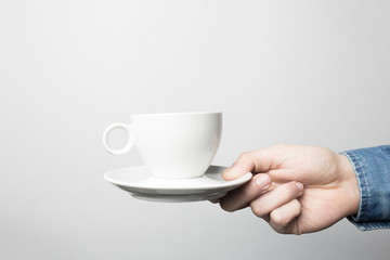 Hand in blue shirt is holding white coffee cup