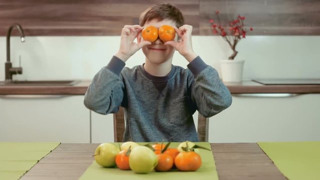 Funny little boy holding mandarins in front of his eyes and having fun