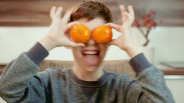 Funny little boy holding mandarins in front of his eyes and having fun