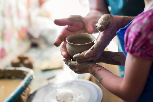 Senior potter teaching a little girl the art of pottery. Child working with clay, Creating ceramic pot on sculpting wheel. Concept of mentorship, generations. Arts lessons, pottery workshop for kids