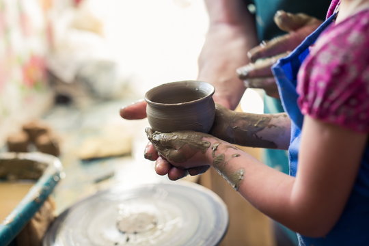 Senior potter teaching a little girl the art of pottery. Child working with clay, Creating ceramic pot on sculpting wheel. Concept of mentorship, generations. Arts lessons, pottery workshop for kids