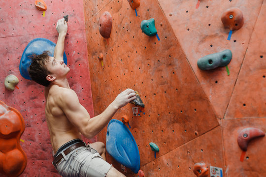 Muscular and fit shirtless man exercise bouldering and climbing indoor at artificial wall