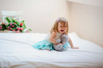 The charming little girl sits on a big bed.