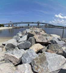 Front view of granite rock jetty with bridge and blue sky in background. Vertical.