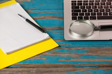 Notepad, pen and magnifying glass with laptop