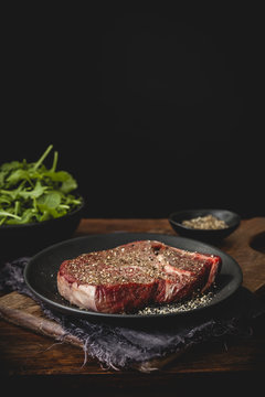 Raw peppered steak on black plate with arugula