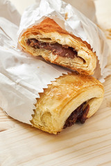 Puff pastry with chocolate filling in white paper bag on wooden background