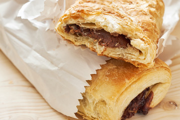 Puff pastry with chocolate filling in white paper bag on wooden background