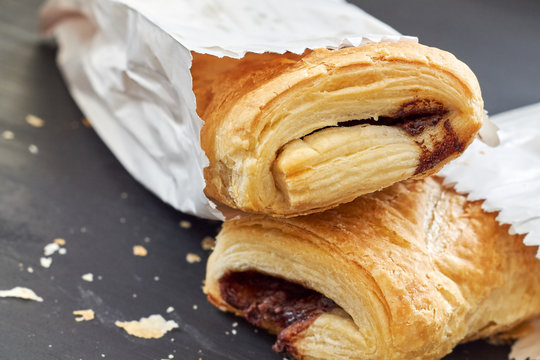 Puff Pastry With Chocolate Filling In White Paper Bag On Black Wooden Background